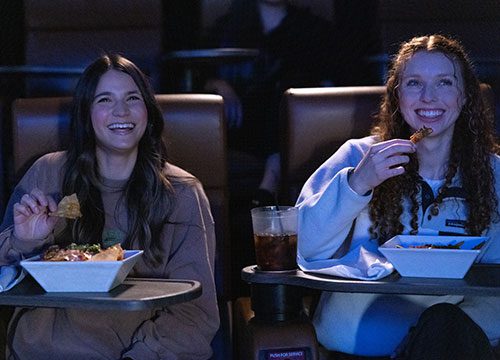 Two women sitting at a movie theater eating food.