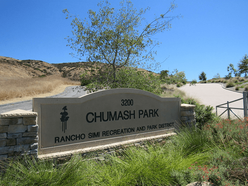 Chumash Park sign with plants and the road in the background