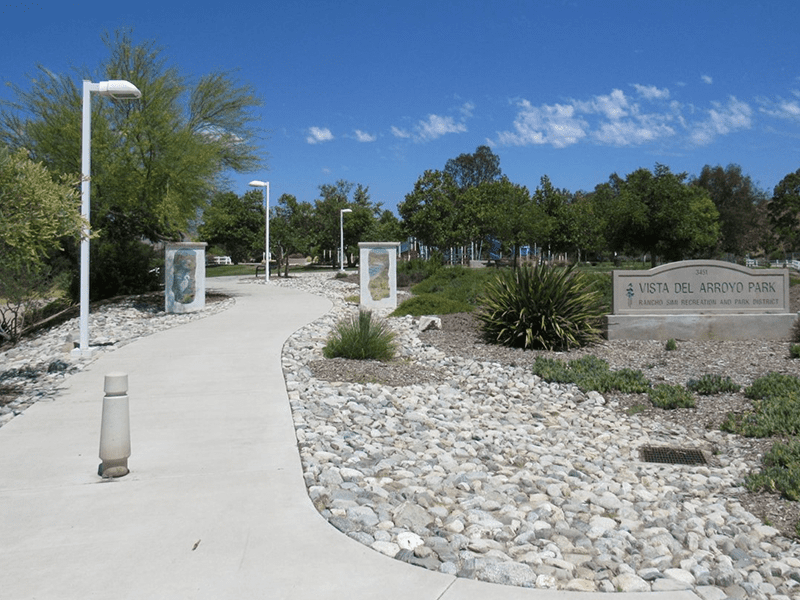 Vista Del Arroyo Park sign with a paved path, rocks, and plants next to it