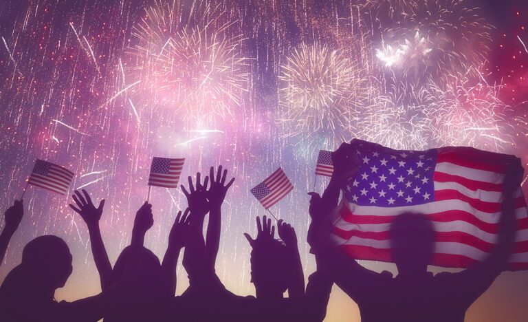 A group of people holding american flags in front of fireworks.
