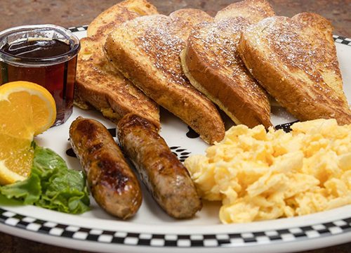 A plate of french toast, sausage, eggs and orange juice.