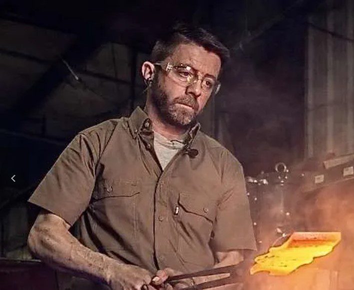 A man wearing safety glasses works with hot metal using tongs in an industrial setting.