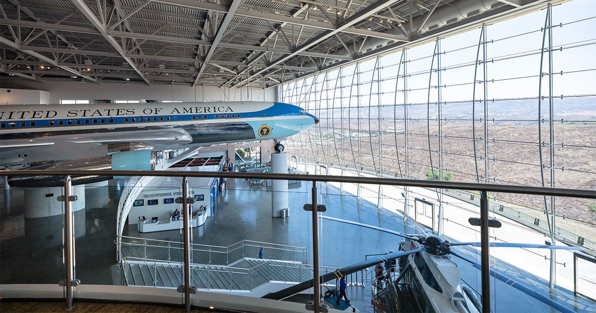 Airplane exhibit inside a large glass-walled museum, featuring a section of a plane with United States of America visible.