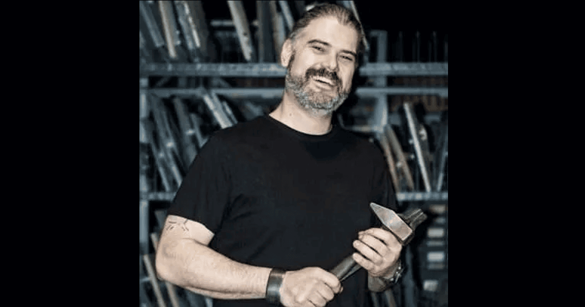 Modern man smiling holding a hammer in a workshop with tools.