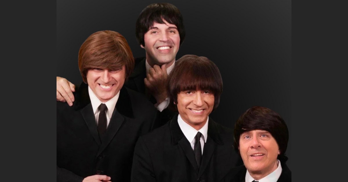 Four men dressed as The Beatles from Liverpool, smiling, in black suits.