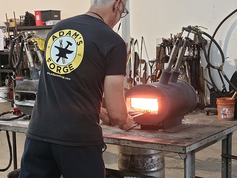 A craftsman working with glassblowing equipment in a studio setting.
