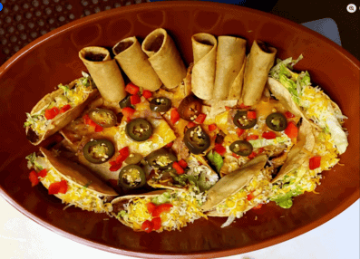 Delicious Mexican food platter with rolled tacos, cheese, olives, and fresh vegetables.