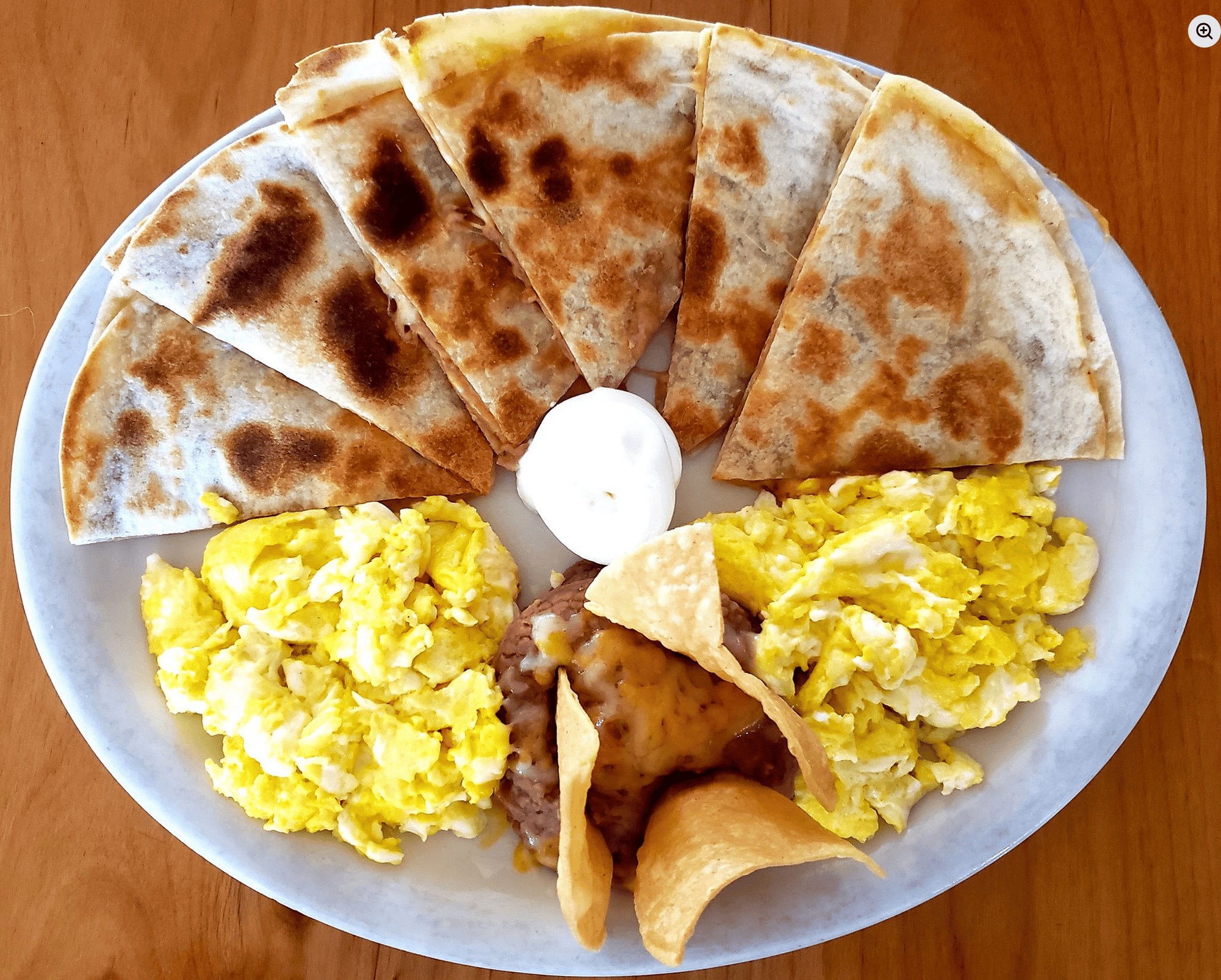 Quesadilla with scrambled eggs, chips, and sour cream on a white plate.