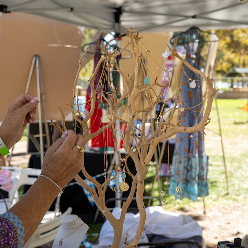 Person displaying handmade jewelry on a tree-shaped stand at Simi Valley event.