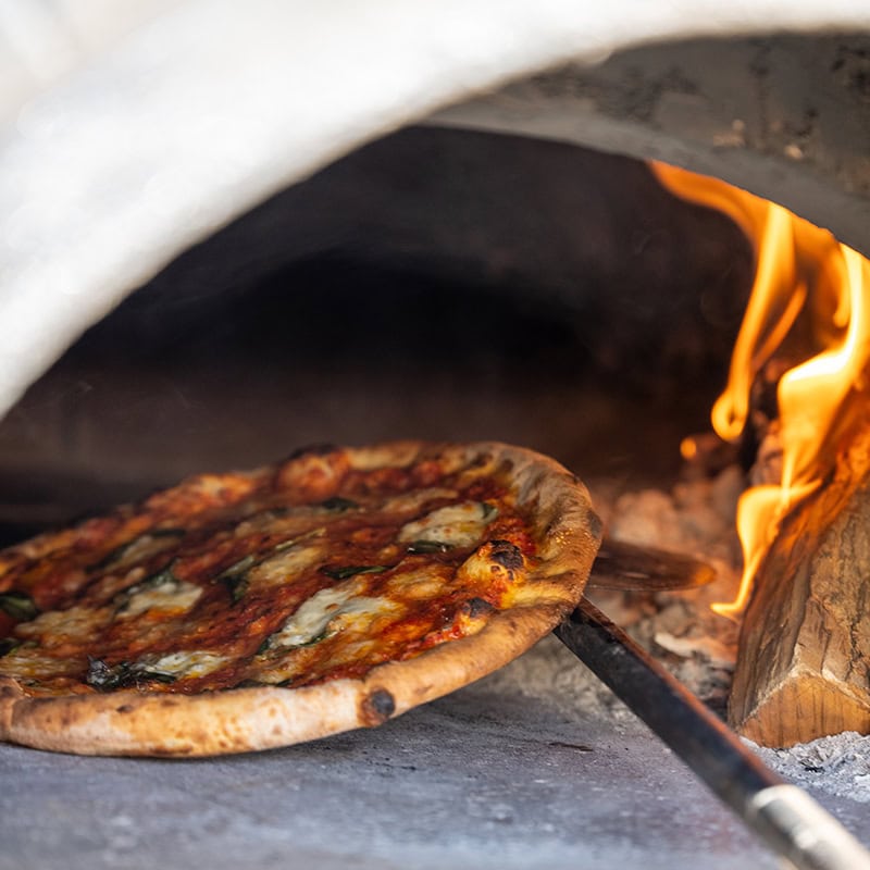 Pizza baking in a wood-fired oven with flames and bubbling cheese.