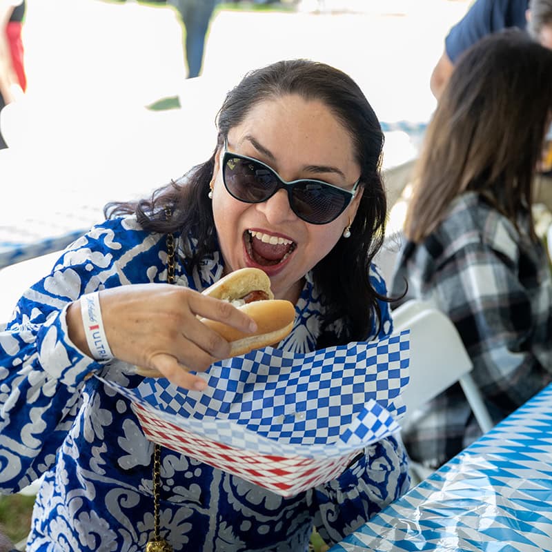 Woman with sunglasses eating hot dog at Oktoberfest celebration in Simi Valley.